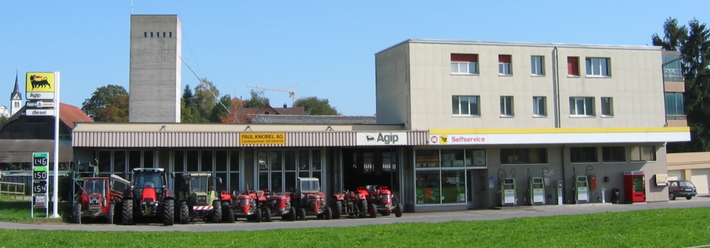 Gebäude der Paul Knobel AG mit AGIP-Tankstelle und einer Reihe Traktoren